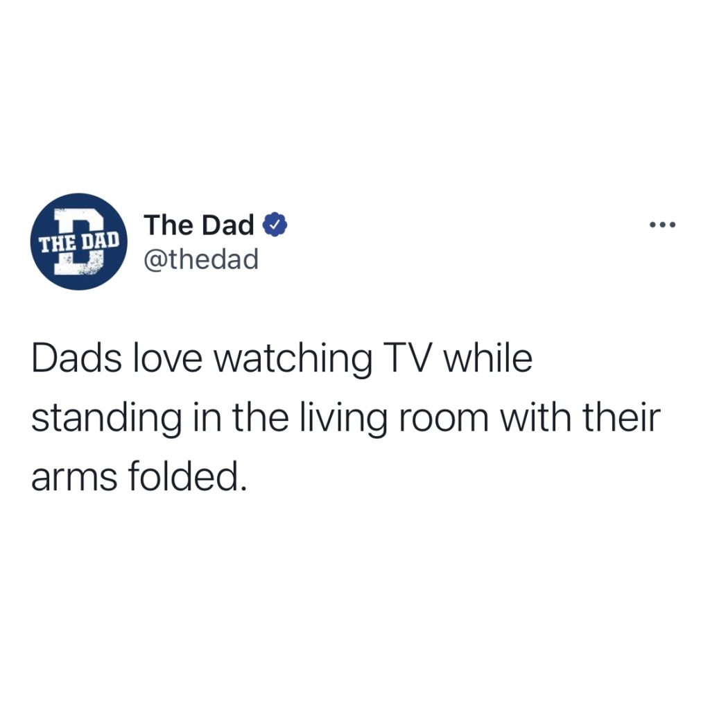 Dads love watching TV while standing in the living room with their arms folded.